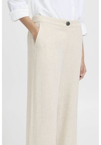 Pantaloni in lino beige con una vestibilità rilassata, tasche laterali e cuciture dettagliate. Presentano una parte frontale piatta e una chiusura con un singolo bottone scuro.