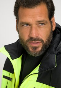 Helle gelbe und schwarze Jacke mit einem Reißverschluss und verstellbarer Kapuze; verfügt über zwei seitliche Taschen und einen strukturierten Stoff.
