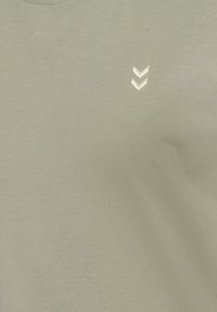 Olivegrön T-shirt med rund halsringning, tillverkad av mjukt material; har en liten, broderad chevron-design i en ljusare färg.