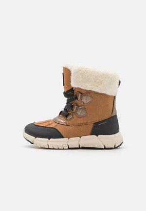 Botín de ante marrón con forro de crema suave, puntera de goma negra y suela texturizada. Presenta tres ojales negros y cordones.