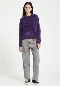 Pull en tricot violet avec une finition texturée et un col rond, associé à un pantalon en denim gris taille haute et des baskets noires.