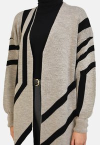 Beige cardigan with black diagonal stripes, open front design, long sleeves, and ribbed cuffs. Made of soft knit fabric. Gold accent belt included.
