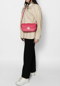 Sac bandoulière en cuir vegan rose avec rabat rabattable et accent métallique. Dispose d'une bandoulière réglable et d'une texture lisse.