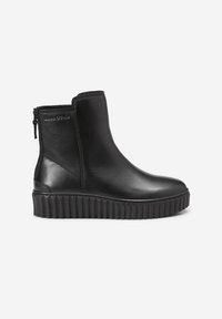 Bottine en cuir noir avec semelle plateforme nervurée, fermeture éclair latérale et logo de marque discret près du bord supérieur.