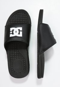 Sorte sandaler med teksturerede gummisåler og en bred rem lavet af syntetisk læder med et hvidt logo. Fladt design til afslappet brug.