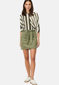 Leichtes gestreiftes Oberteil in Grün und Creme, kombiniert mit einem figurbetonten, grünen Wildlederrock mit einem Bindegürtel und seitlichen Taschen. Weiße Sneakers runden den Look ab.
