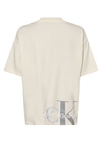 Krémové oversized tričko s žebrovaným výstřihem. Na zadní straně se nachází velké grafické logo v modré a černé barvě s názvem značky.