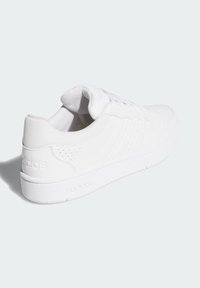 Biele tenisky so hladkým syntetickým zvrškom, šnurovacie uzatváranie a perforované detaily. Majú plochú gumovú podrážku a embosované logo.