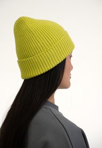 Gorro de punto amarillo con textura acanalada y parte superior puntiaguda, llevado con un sudadera gris, mostrando el perfil lateral de la cabeza.