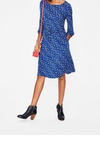 Blommig klänning i blått med trekvartslånga ärmar, åtdragen vid midjan. Matchas med svarta anklarstövlar med texturerad klack och sidodragkedja.