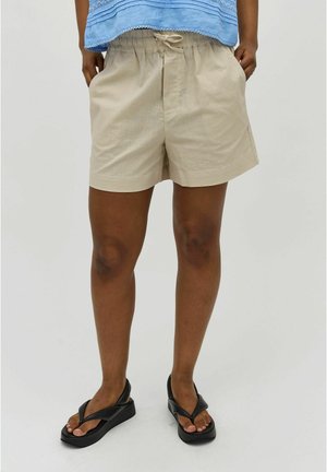 Beige shorts with an elastic waistband, side pockets, and a relaxed fit, paired with black flip-flop sandals on bare feet.