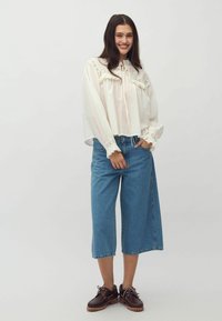 White, long-sleeve blouse with lace detailing, paired with light blue, wide-leg denim culottes and dark brown lace-up shoes.
