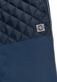 Jachetă cu model matlasat de culoare navy, cu modele în formă de diamant și o secțiune inferioară netedă. Include o etichetă mică cu logo-ul mikk-line pe material.