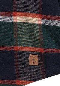 Tessuto a quadri in tonalità di blu scuro, verde e rosso con etichetta in pelle color crema che mostra il logo "Key Largo". Texture morbida con un aspetto simile alla lana.