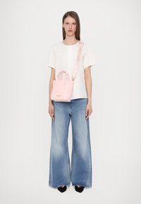 Mini rosa handväska med två axelremmar och en avtagbar rem; bärs med en vit topp och vida blå jeans; svarta skor.