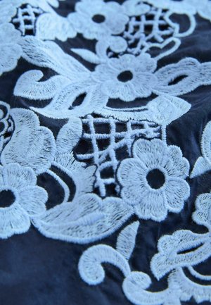 Navy fabric featuring intricate light blue floral embroidery with vines and lace-like patterns. Soft texture with detailed stitching.