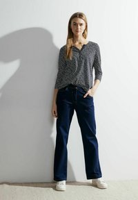 Czarny i biały wzorzysty top z rękawami o długości trzech czwartych, zestawiony z ciemnoniebieskimi dżinsami i białymi trampkami. Prosty, luźny krój.
