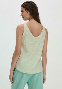 Helles grünes Trägershirt mit V-Ausschnitt und feinen horizontalen Streifen, ausgestattet mit einer weichen Textur und einem kontrastierenden cremefarbenen Besatz entlang des Ausschnitts.