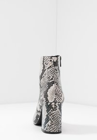 Snake-print ankle boot with a textured surface, black heel, and zipper closure, featuring a glossy finish in shades of gray and cream.