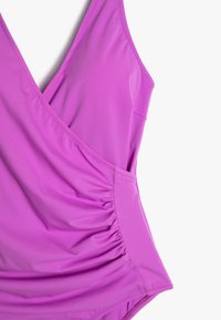 Maillot de bain une pièce violet fabriqué à partir d'un matériau lisse et élastique. Doté d'un design à l'avant tordu et de côtés froncés pour un look ajusté.