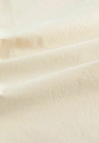 Tissu doux de couleur crème avec des plis délicats et une surface lisse légèrement texturée.