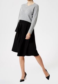 Szary sweter dzianinowy z dekoltem w kształcie litery V, w połączeniu z czarną spódnicą w kształcie litery A z wiązanym pasem. Założone z czarnymi szpilkami.