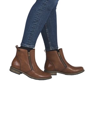 Brown leather ankle boots with a side zipper, rounded toe, and a low stacked heel, paired with blue denim jeans.