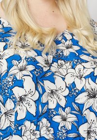 Haut fleuri avec un fond bleu et des fleurs blanches et noires. Tissu léger et texturé, coupe décontractée et manches courtes.