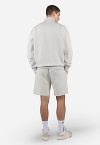 Pullover grigio chiaro con colletto alto, abbinato a pantaloni corti coordinati. Il materiale appare morbido, con un design semplice e una vestibilità comoda.
