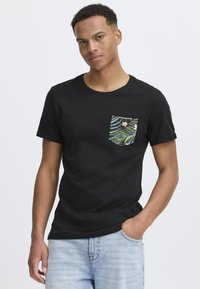Camiseta corta de manga negra con un bolsillo que presenta un patrón tropical multicolor. Material de algodón, escote redondo y corte relajado.