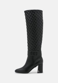 Bota negra hasta la rodilla con parte superior acolchada, banda ancha y detalle de logo, tacón cuadrado con acento metálico y área del dedo del pie lisa.