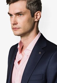 Granatowa marynarka na różowo-białą w paski koszulę. Marynarka ma przypinkę na klapie i gładką teksturę, podczas gdy koszula ma klasyczny kołnierz i guziki.