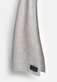 Jasnoszary szal z kaszmiru o miękkiej fakturze, w kształcie prostokąta. Posiada czarną metkę z białym napisem.