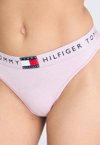 Rózsaszín pamut tanga, kontrasztos derékrésszel, amelyen a "TOMMY HILFIGER" felirat és egy logopatch található. Simogatós textúra, minimális fedettségű dizájn.
