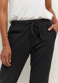 Schwarze Hosen mit elastischem Bund, verstellbarem Kordelzug, Seitentaschen und lockerer Passform aus weichem Stoff.