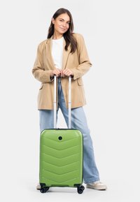 Tvrdý zelený kufr s chevronov�ým vzorem, teleskopická stříbrná rukojeť a čtyři černá kola. Pozadí je bílé.