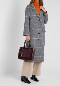 Gråternet lang frakke, orange turtleneck, creme brede bukser, sorte blanke hælede støvler og en burgunder håndtaske med tekstureret detalje.