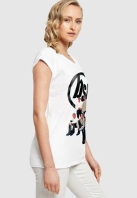 Tricou alb cu guler rotund și mâneci scurte, având un imprimeu grafic cu șase persoane într-un logo cerc negru.