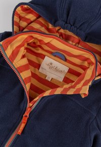 Fleecejacke mit einem marineblauen Außenmaterial und einem orange gestreiften Innenfutter. Verfügt über einen Frontreißverschluss und ein Etikett mit Markenname und Größe.