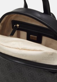 Sac à dos noir à motifs avec un extérieur lisse, une fermeture éclair, et un intérieur beige agrémenté de quincaillerie dorée et d'une poche interne.