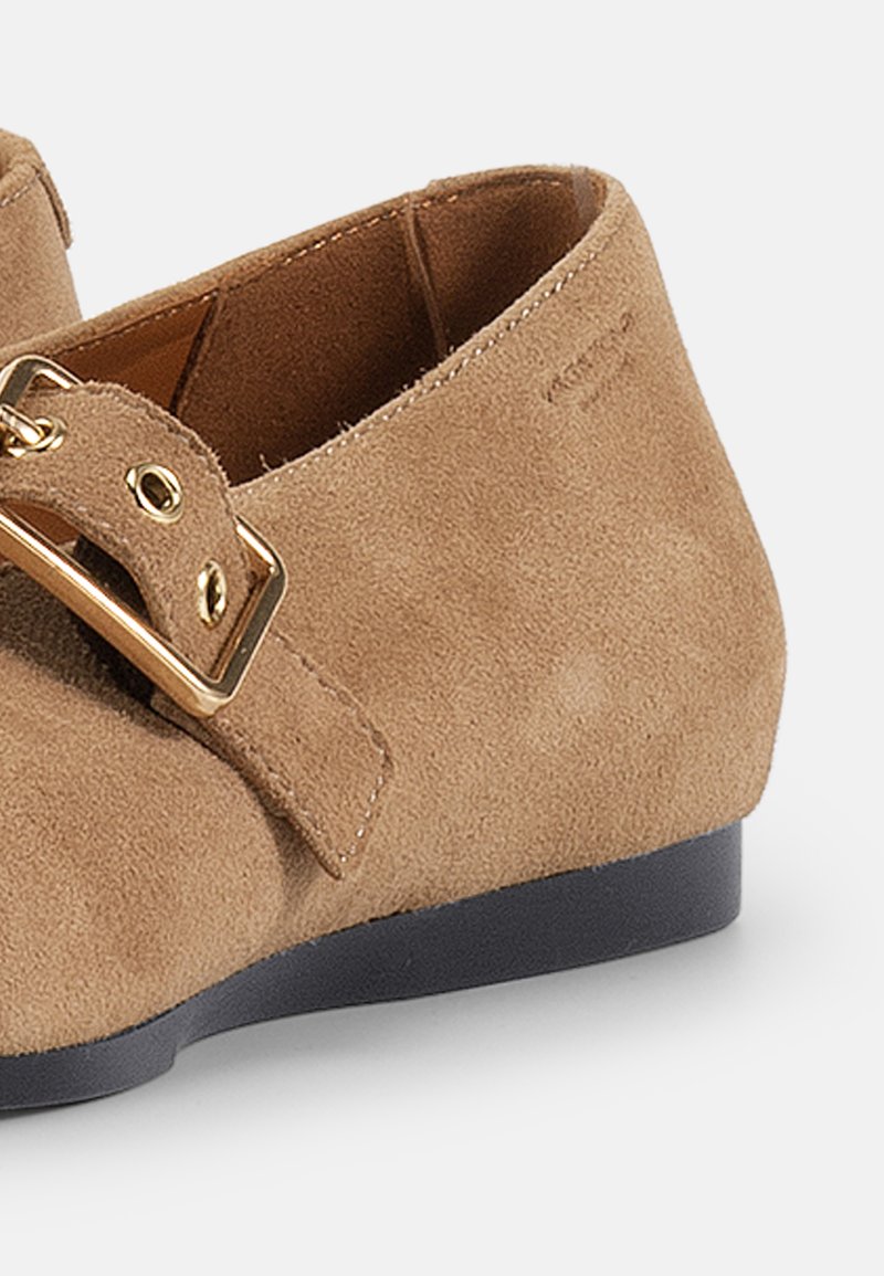 Jasnobrązowe zamszowe buty z okrągłym noskiem, płaską czarną podeszwą oraz szerokim paskiem z detalem złotego zapięcia.