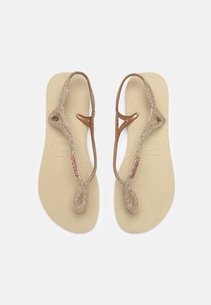 Brune flip-flops med glitrende guldremme. Remmene har et snoet design og en dekorativ detalje. Struktureret sål for bedre greb.