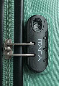 El material texturizado verde de la maleta presenta herrajes en negro, incluyendo tiradores de doble cremallera y un candado con la marca "ITACA".