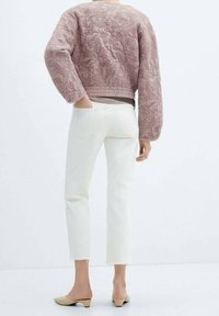 Giacca bomber trapuntata rosa chiaro con design floreale, abbinata a jeans bianchi a vita alta e mule beige. Presenta una texture morbida e polsini aderenti.