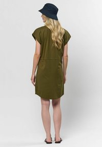 Rochie scurtă, de culoare verde măsliniu, cu mâneci scurte, talie strânsă, tiv rotunjit și țesătură moale, asortată cu o pălărie tip bucket neagră și sandale negre.