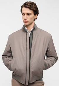 Ανοιχτό γκρι μπουφάν bomber με κλείσιμο με φερμουάρ, ριμπ μανσέτες και πλαϊνές τσέπες. Λείο ύφασμα με μοντέρνο σχεδιασμό.