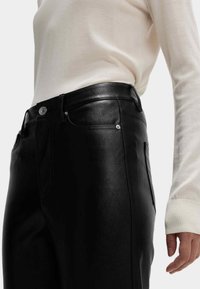 Černé kalhoty z umělé kůže s hladkým povrchem, vysokým pasem a jemným stříbrným hardwarem. Nositelka kombinovala s krémovým svetrem.