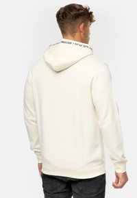 Crème-kleurige hoodie met een kangoeroezak, ribgebreide boorden en een capuchon met trekkoord. De binnenvoering heeft een contrasterend tekstpatroon.
