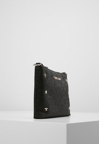 Sac paillettes noires avec des clous en forme d'étoiles argentées, une fermeture éclair et une forme rectangulaire élégante. Le matériau a une texture lisse avec des accents brillants.