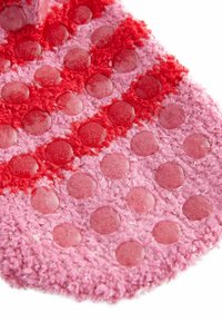 Texturiertes rosa Stoff mit runden Silikon-Griffpunkten in verschiedenen Rosa- und Rottönen. Der Stoff hat ein weiches, flauschiges Aussehen.